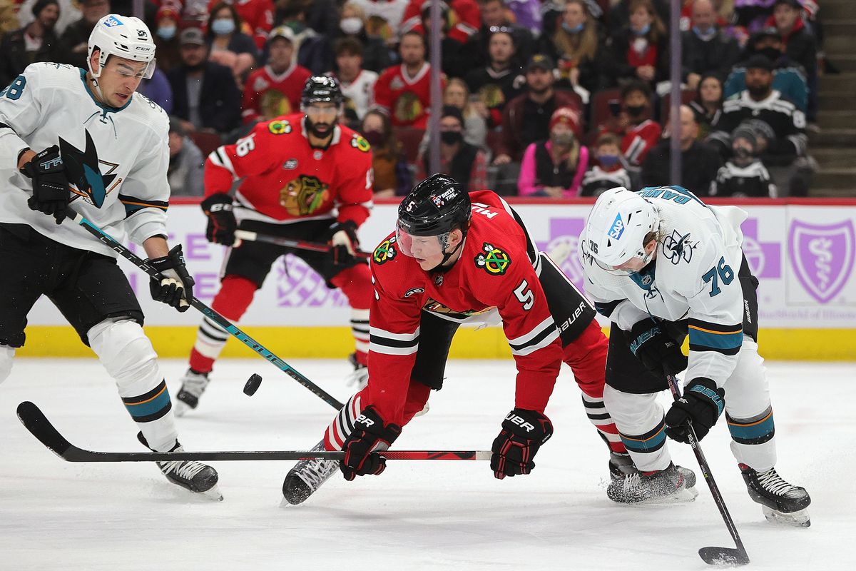 Connor Murphy #5 of the Chicago Blackhawks tries to control the puck between Timo Meier #28 and Jonathan Dahlen #76 of the San Jose Sharks at the United Center on November 28, 2021 in Chicago, Illinois.