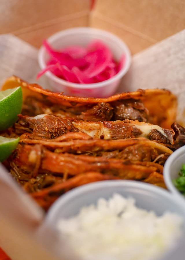 Three birria tacos with a side of pickled red onions and a wedge of lime at Taqueria Jalisco.