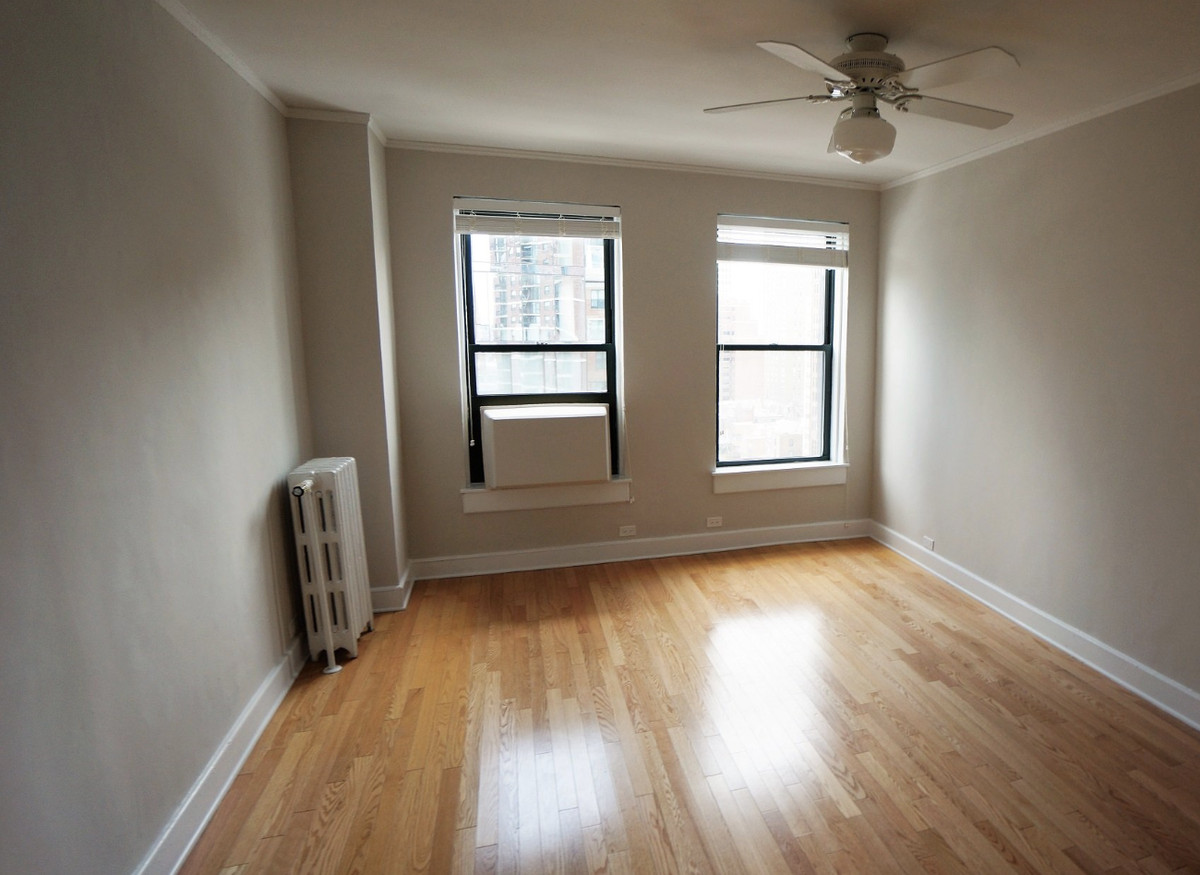 A view of the bedroom with a radiator, two windows, and hardwood floors.