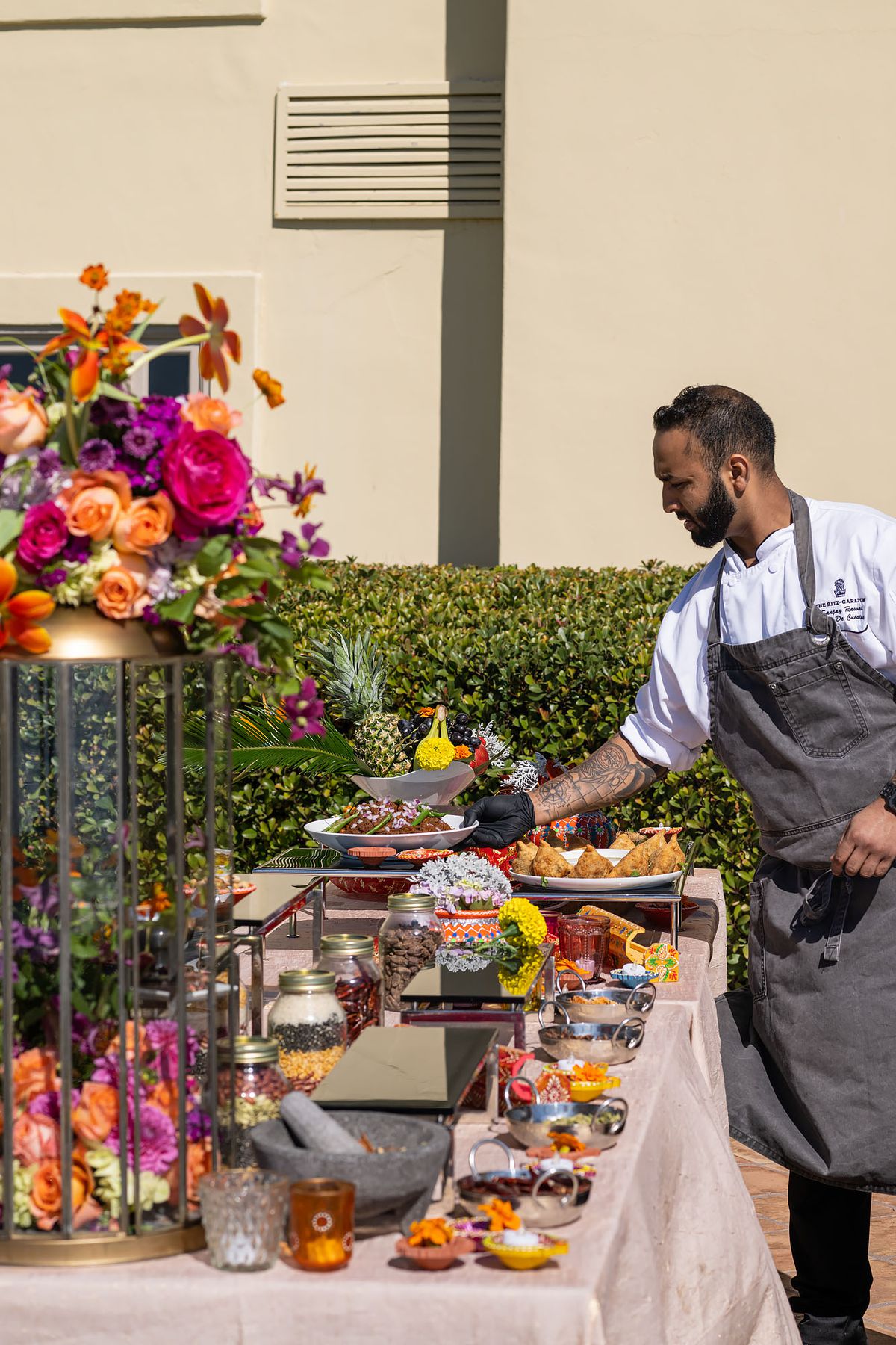 A man of Indian descent places a prepared dish onto a colorful buffet spread.