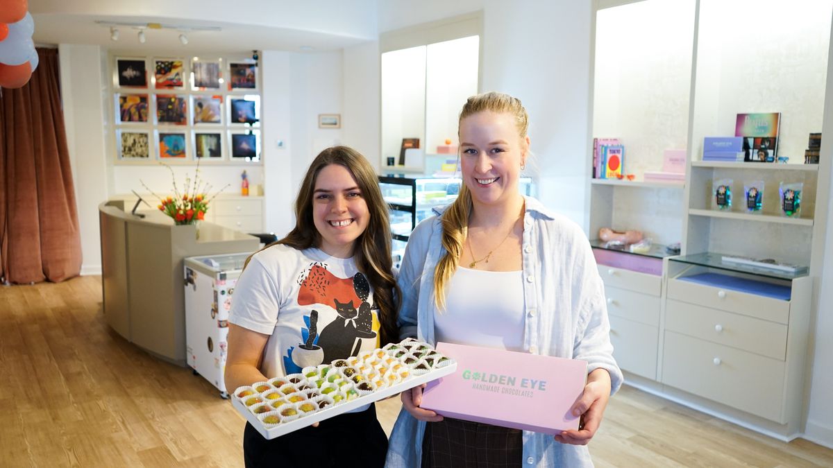 Two women holding up boxes of chocolates in a store.