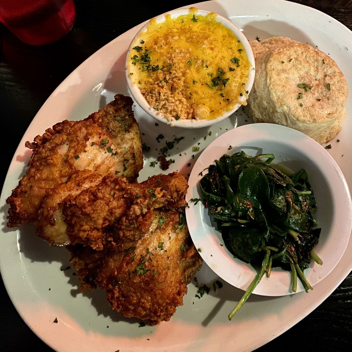 A plate of fried chicken with a biscuit, mac n cheese, and spinach.