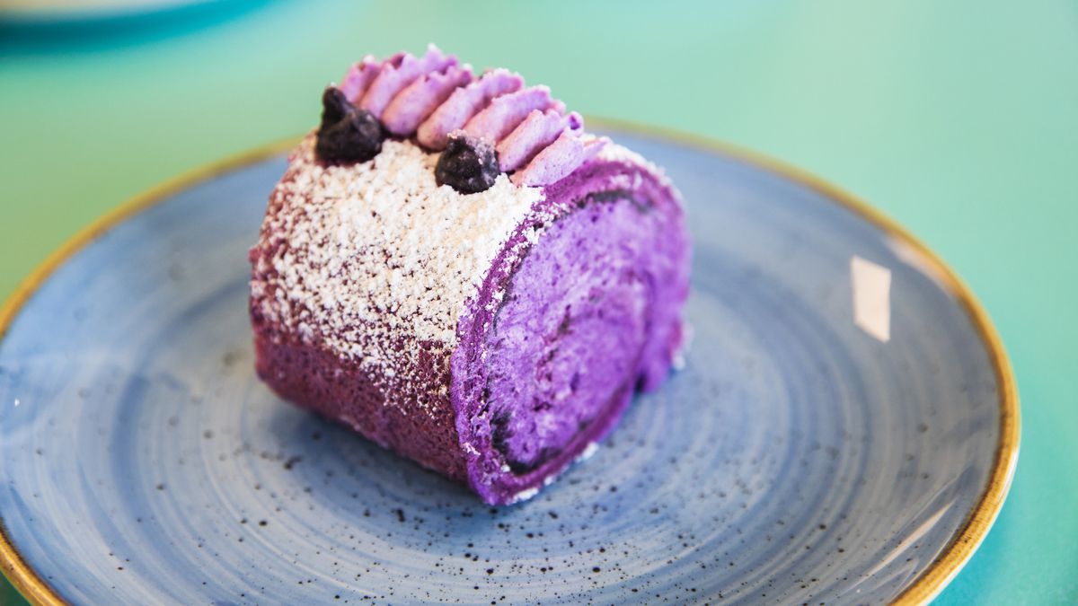 A purple cake roll topped with powdered sugar and blueberries.