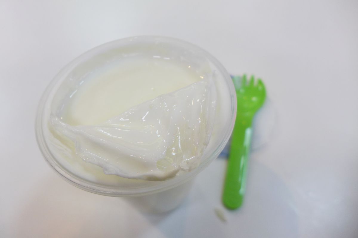A plastic glass filled with white, with a green blurry spoon on the side.