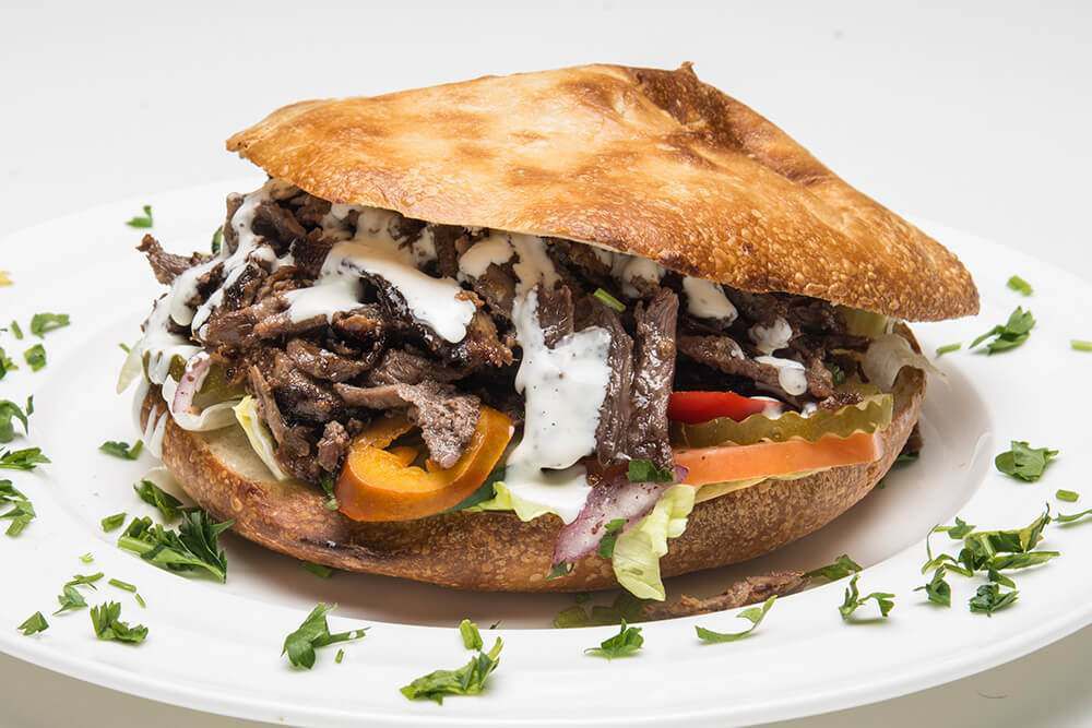 A sandwich stuffed with meat and drizzled with white sauce. The bread is a golden pita sliced in half. 