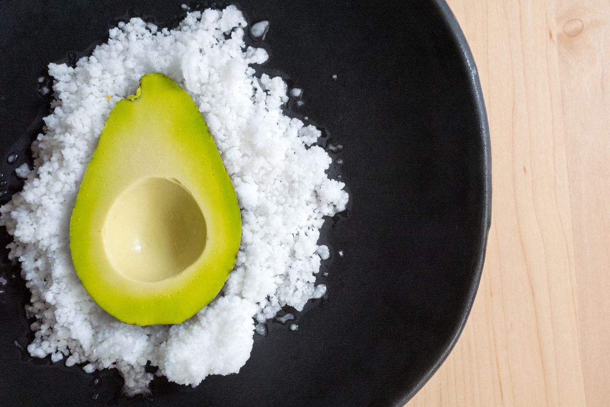 An avocado&nbsp;and lime purée, eucalyptus yogurt, and lime snow plated on a black dish and set on a light wooden table.