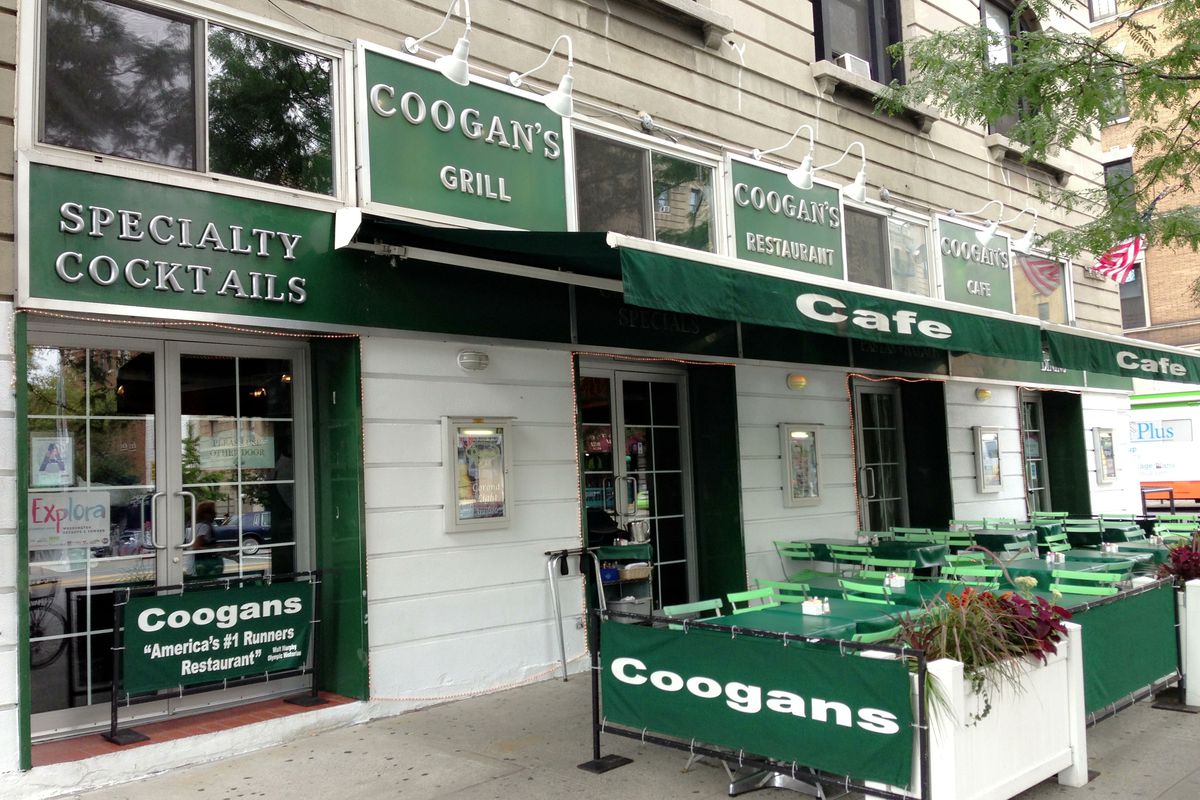 The front of an Irish pub in Washington Heights, New York. Green signs with white lettering say “Coogan’s” on them