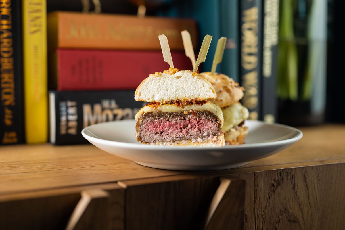 A medium-rare burger with a layer of cheese is served in a bun stuck with two toothpicks and cut in half.
