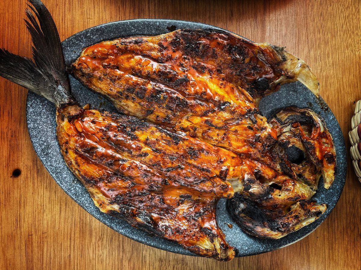 From above, a butterflied grilled fish on a stone dish on a wooden table
