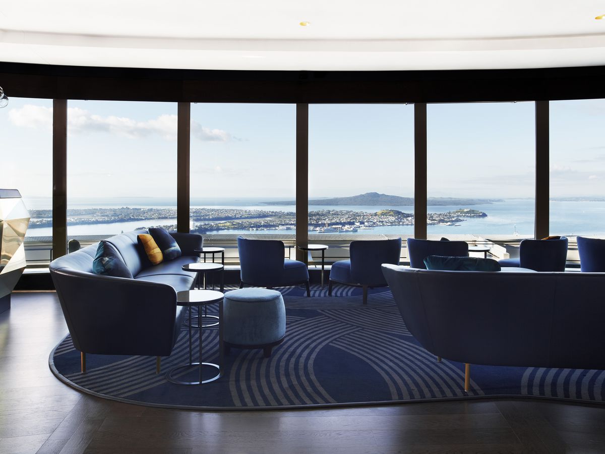 A lounge with couches and low seats overlooking a sky-high view of the city and water.