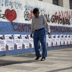 A pedestrian walks by a wall covered in election campaign posters and graffiti in Caracas, Venezuela, Friday, April 12, 2013. Interim President Nicolas Maduro,who served as Chavez's foreign minister and vice president, is running against opposition candidate Henrique Capriles in Sunday's presidential election. (AP Photo/Ariana Cubillos)