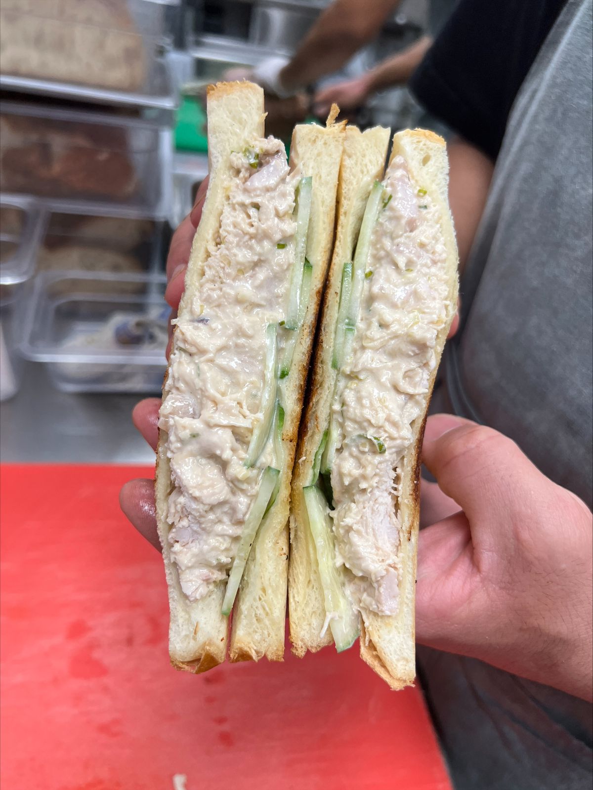 Hands holding a white bread sandwich with chicken salad and cucumbers.