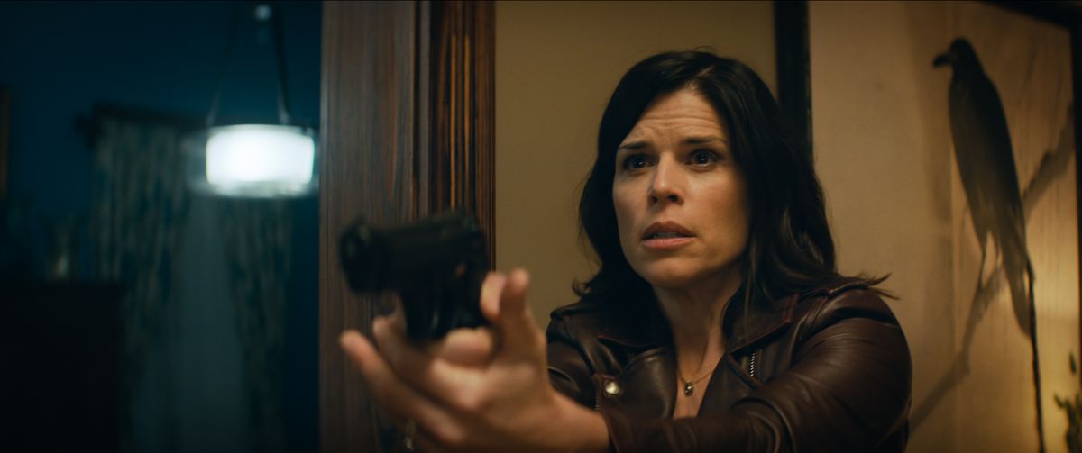 A freaked-out-looking Neve Campbell points a gun offscreen in the 2022 Scream