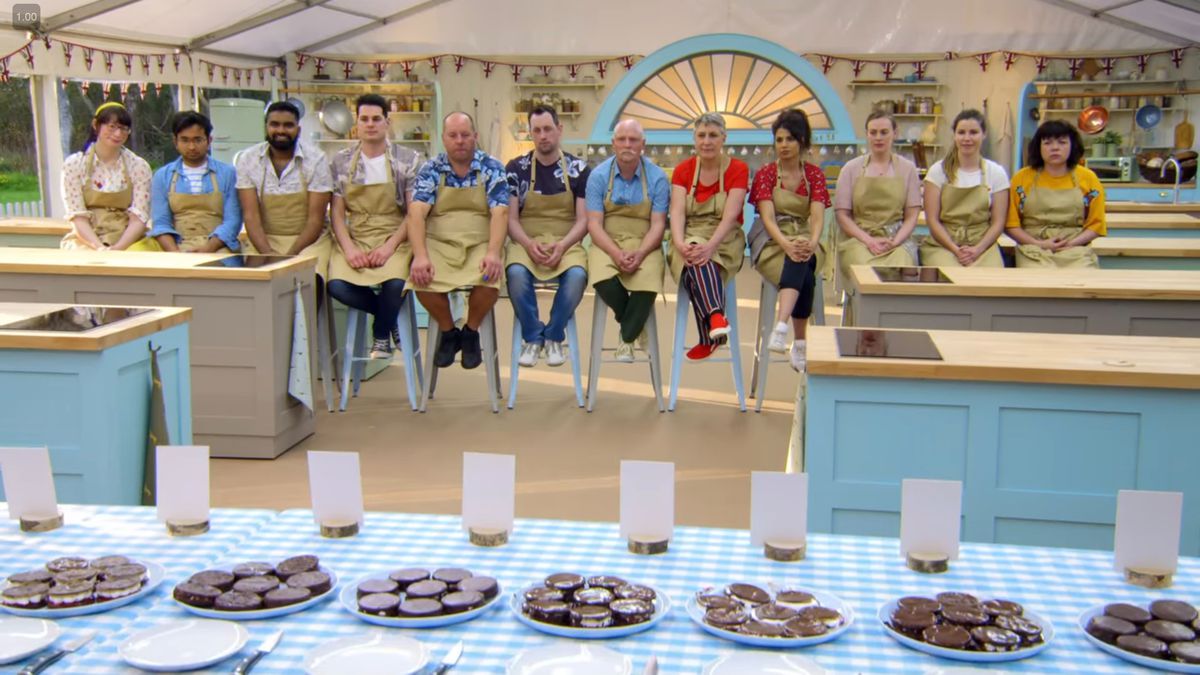 The cast of Great British Bake Off season 9 sitting in a row during the judging of a technical challenge where they were asked to bake wagon wheels.