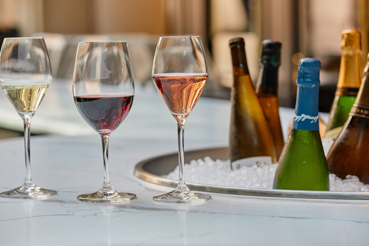 Several glasses of wine are lined up on a bar next to a tub of wine bottles on ice.