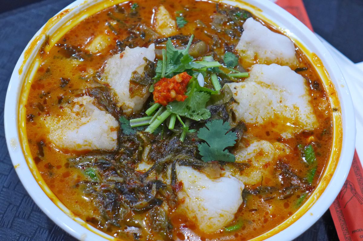 A bowl of bright red soup with clumps of fish.