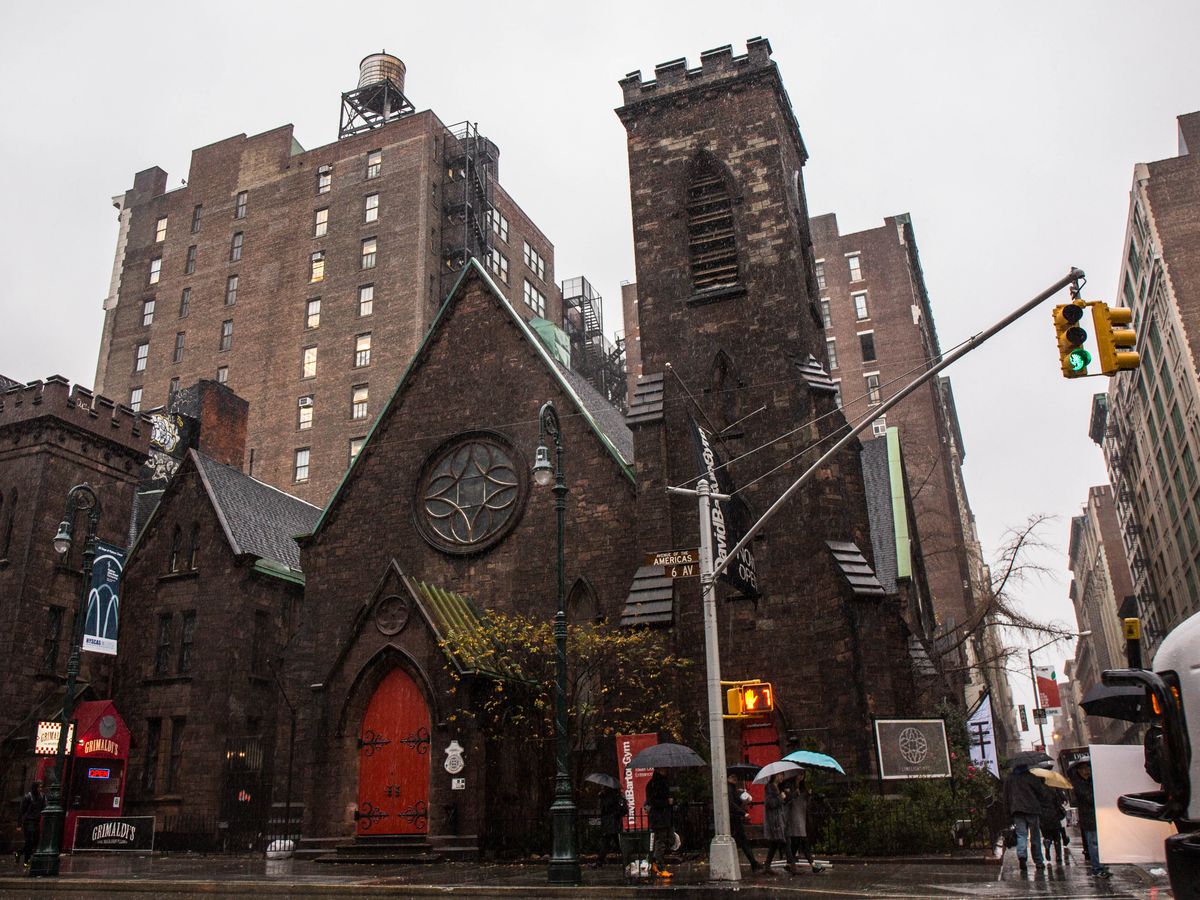 A church on the corner of a city block surrounded by apartment buildings. The church has a red door.