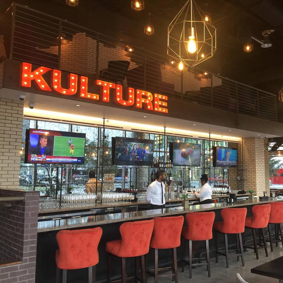 The bar at Kulture with blush seating, TVs, and its name “Kulture.”
