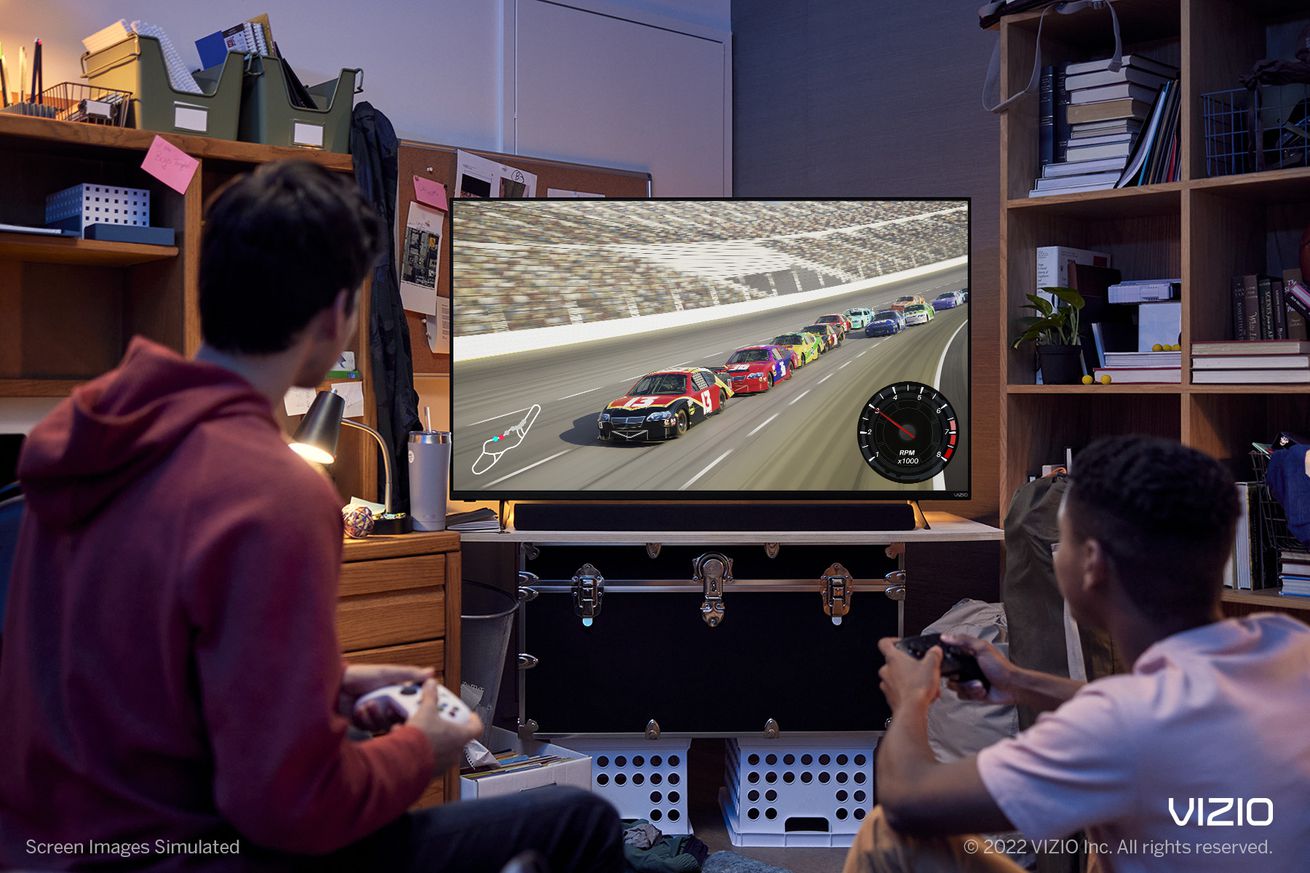 Two people play a racing game on a Vizio TV.
