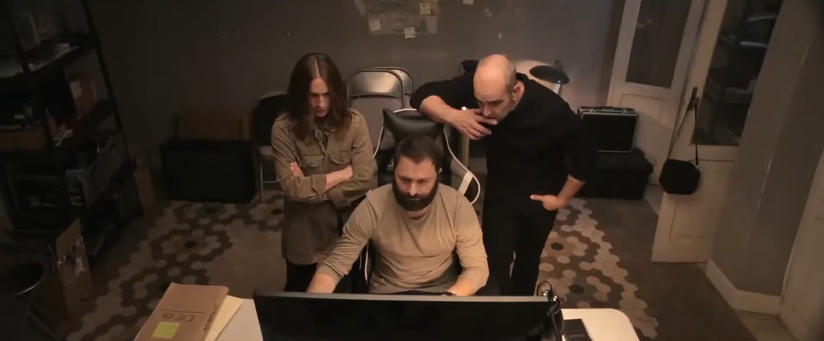 Tres personas se paran alrededor de una computadora en Code Name: Emperor.