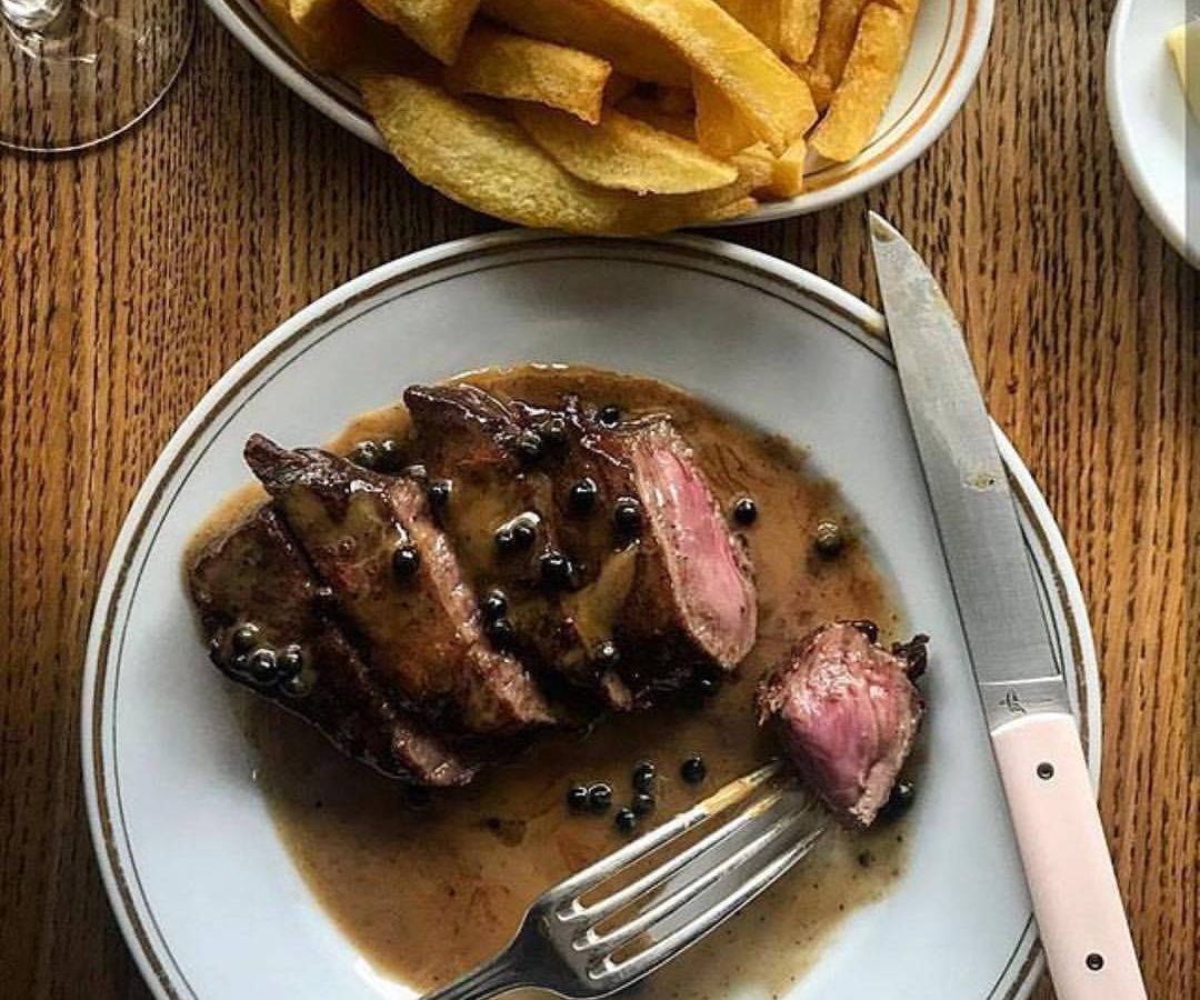 From above, a plate of sliced stake with fork and knife beside a separate plate of thick-cut fries