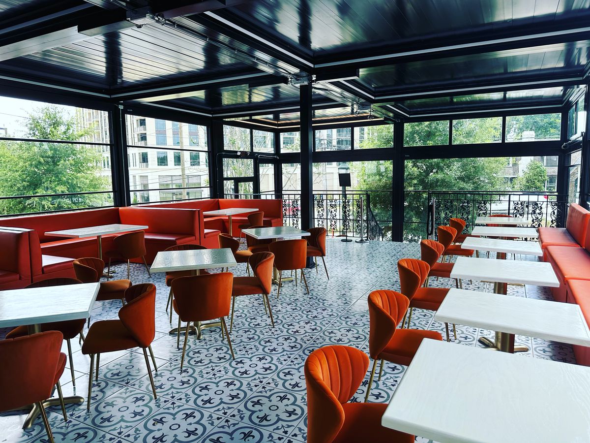 The enclosed glass patio with decorative blue and white tiles on the floor, white tables and plush orange velvet chairs at Bar Ti Amo in Buckhead Atlanta. 