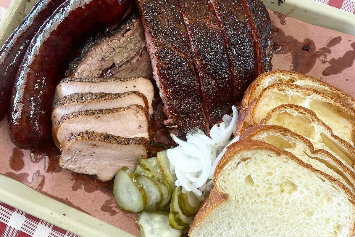 A spread of barbecued meats, including sausage, smoked turkey, ribs, onions, pickles, and slices of white bread.