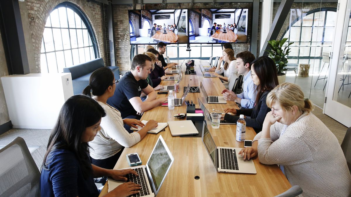 People sit at a long conference table, each with their own laptop in front of them.