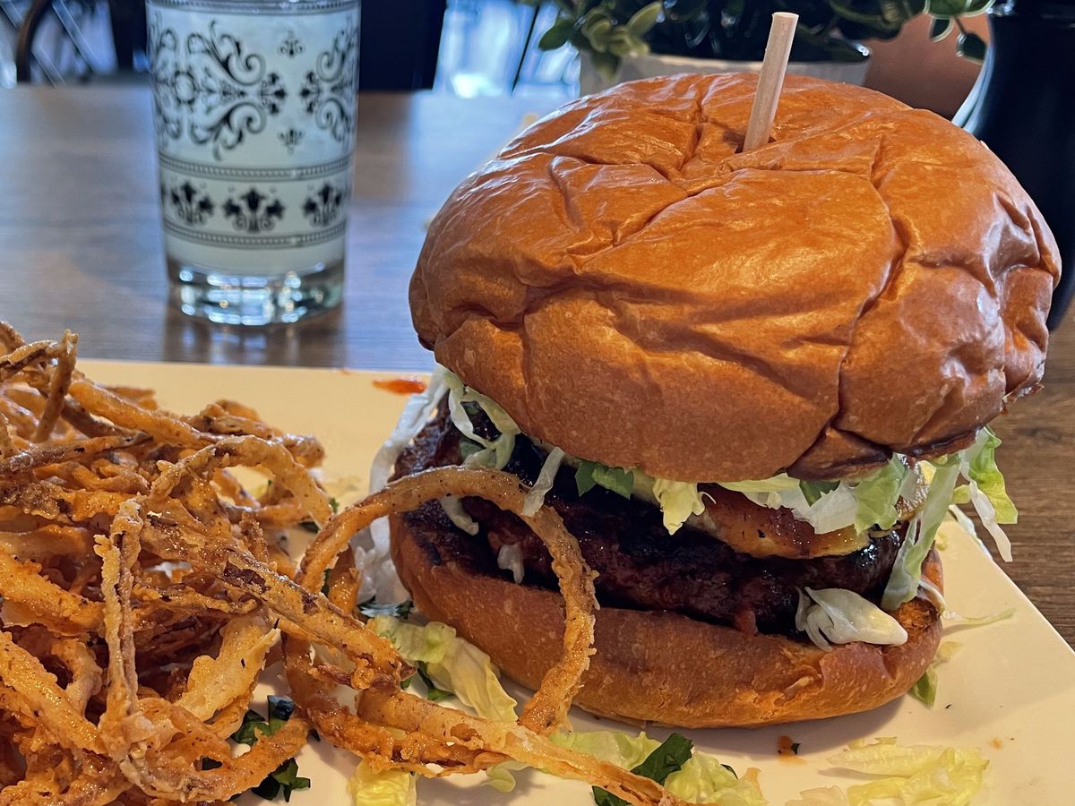 A burger with a pile of fried onions. 