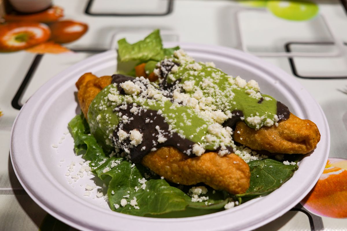Two large fried dumplings topped with black beans, avocado sauce, and cheese.