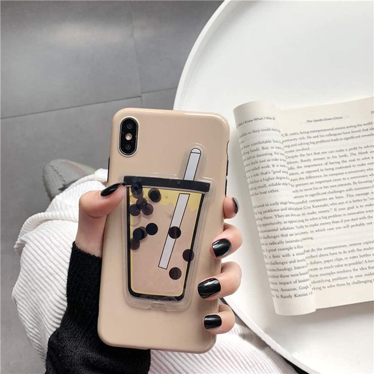 A hand holds a phone case with the image of a cup of bubble tea on the bac