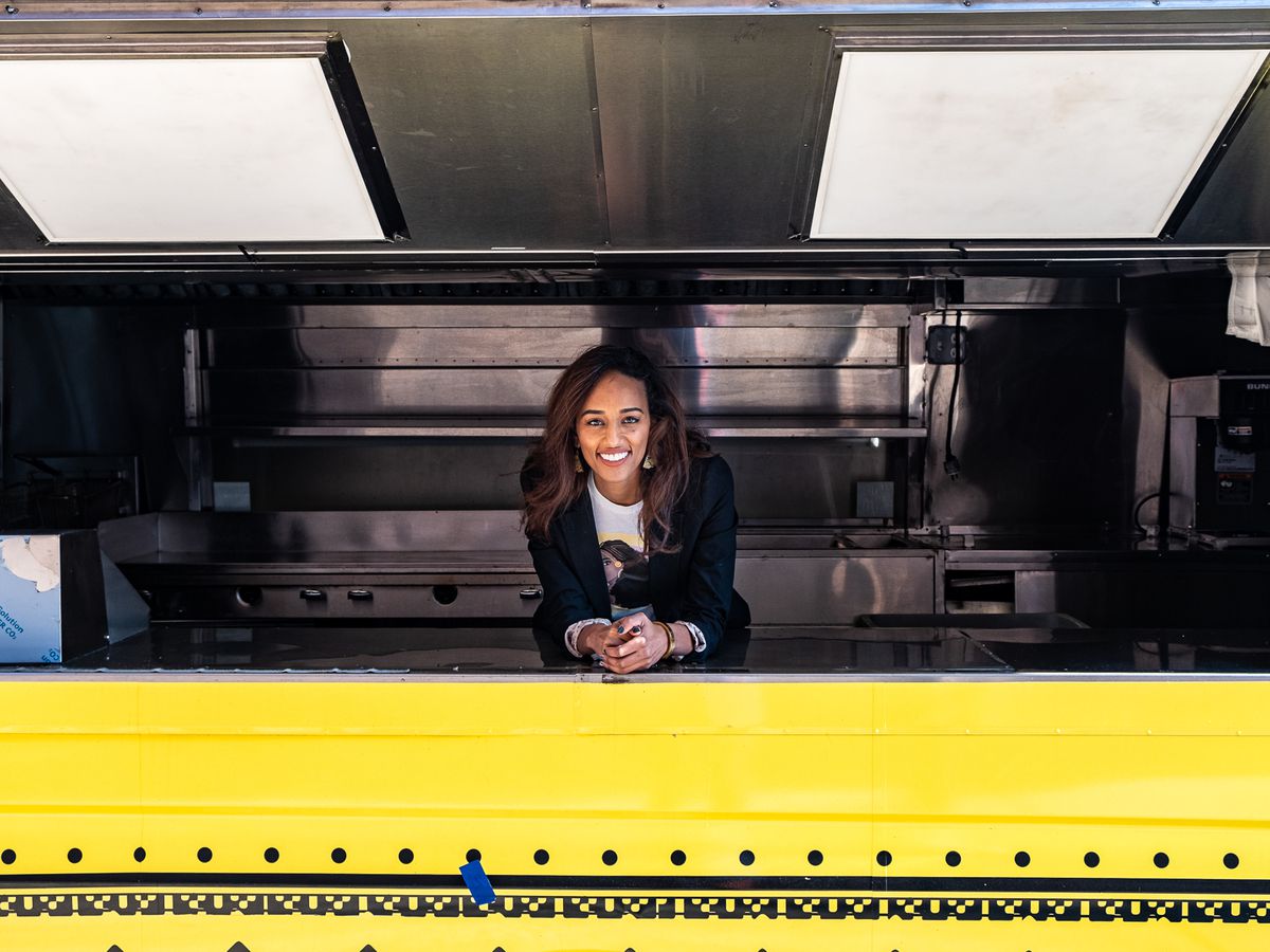 A person, Eden Gebre Egziabher, is pictured leaning over the counter of a yellow food truck.