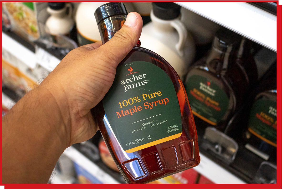 Hand holding bottle of maple syrup in a grocery aisle.