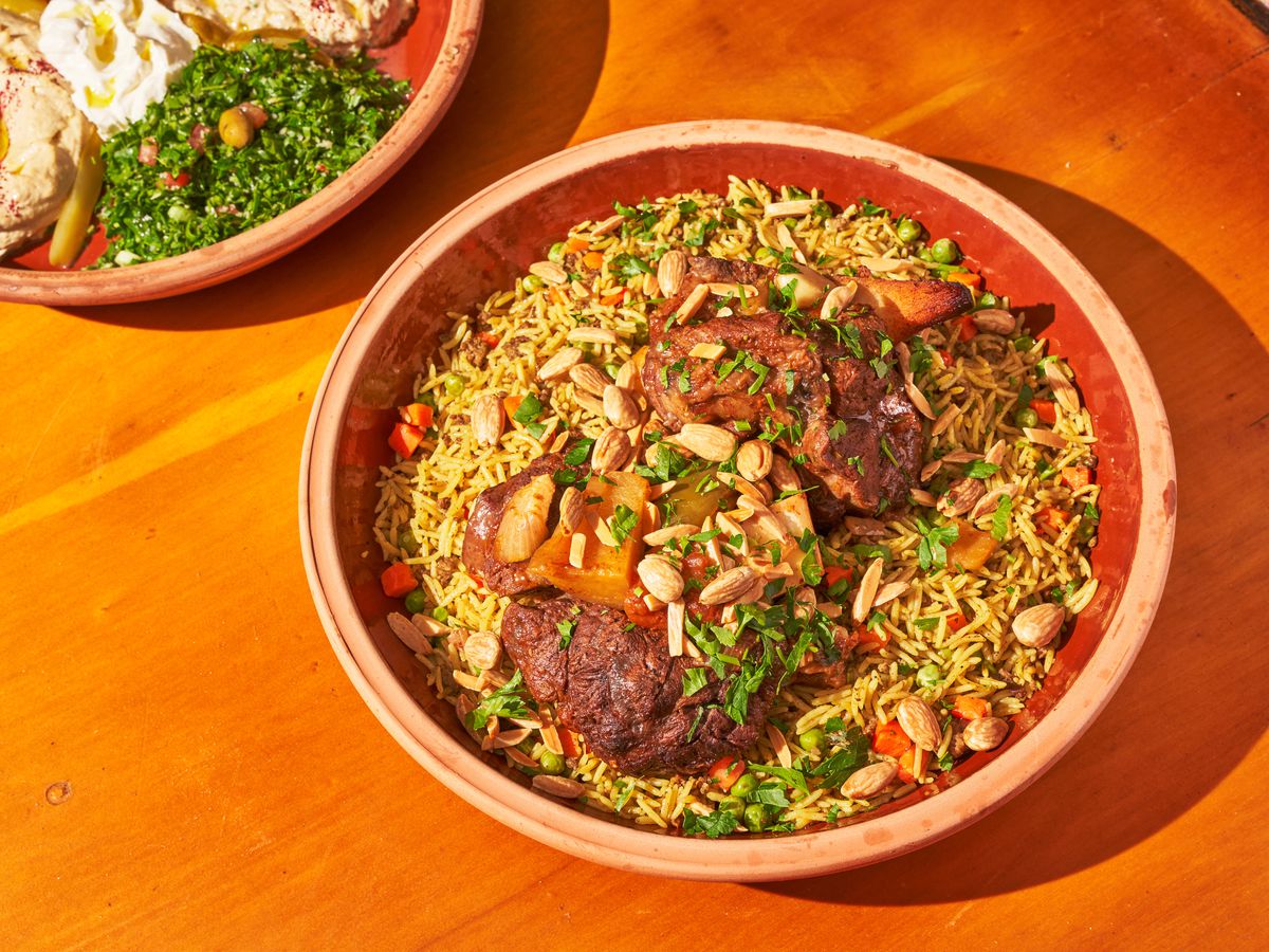 beef, yellow rice, almond slices and a herb garnish are served in a terracotta bowl on a wood table.