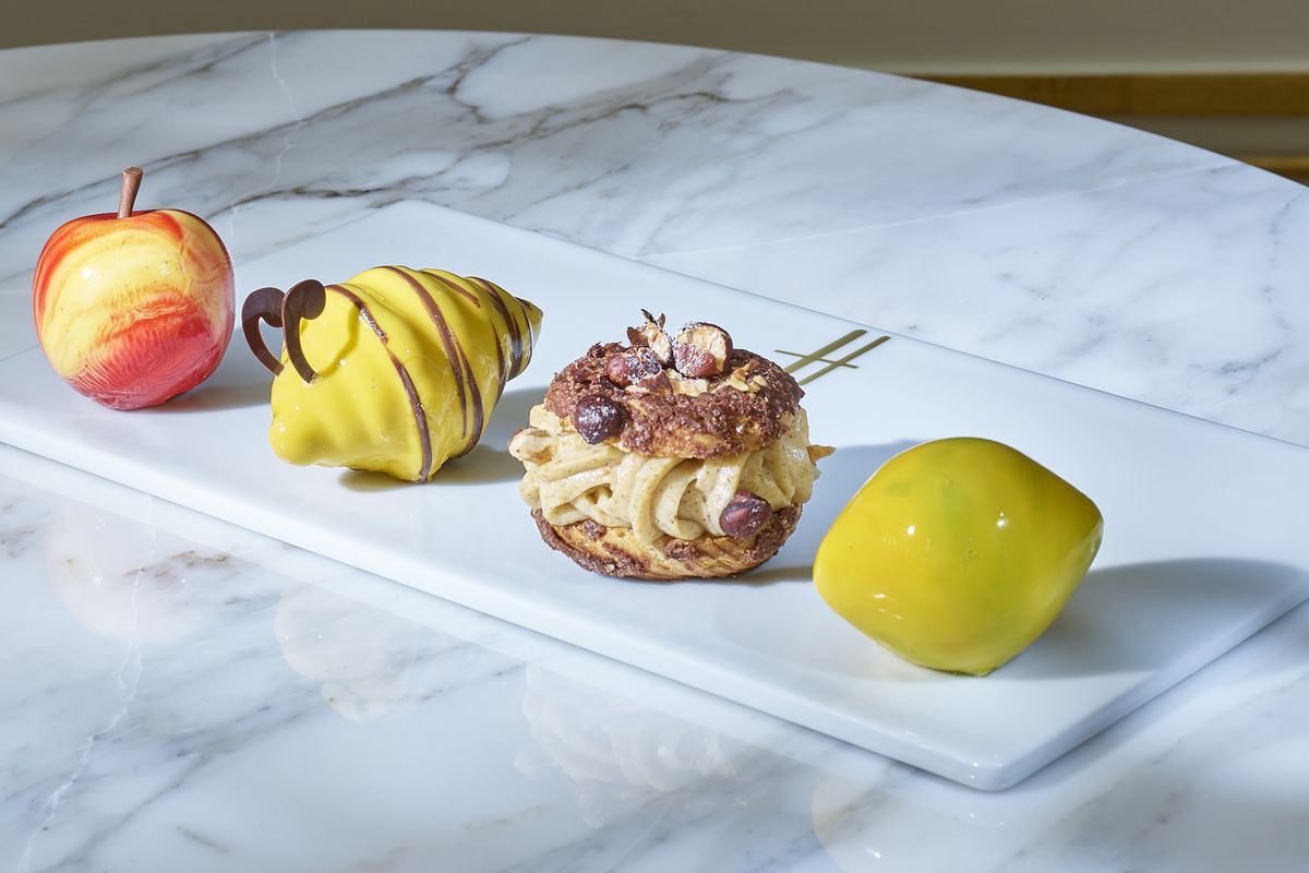 A trio of sculpted patisserie fruits — and one choux — by Cédric Grolet, on a white plate, on a marble table.
