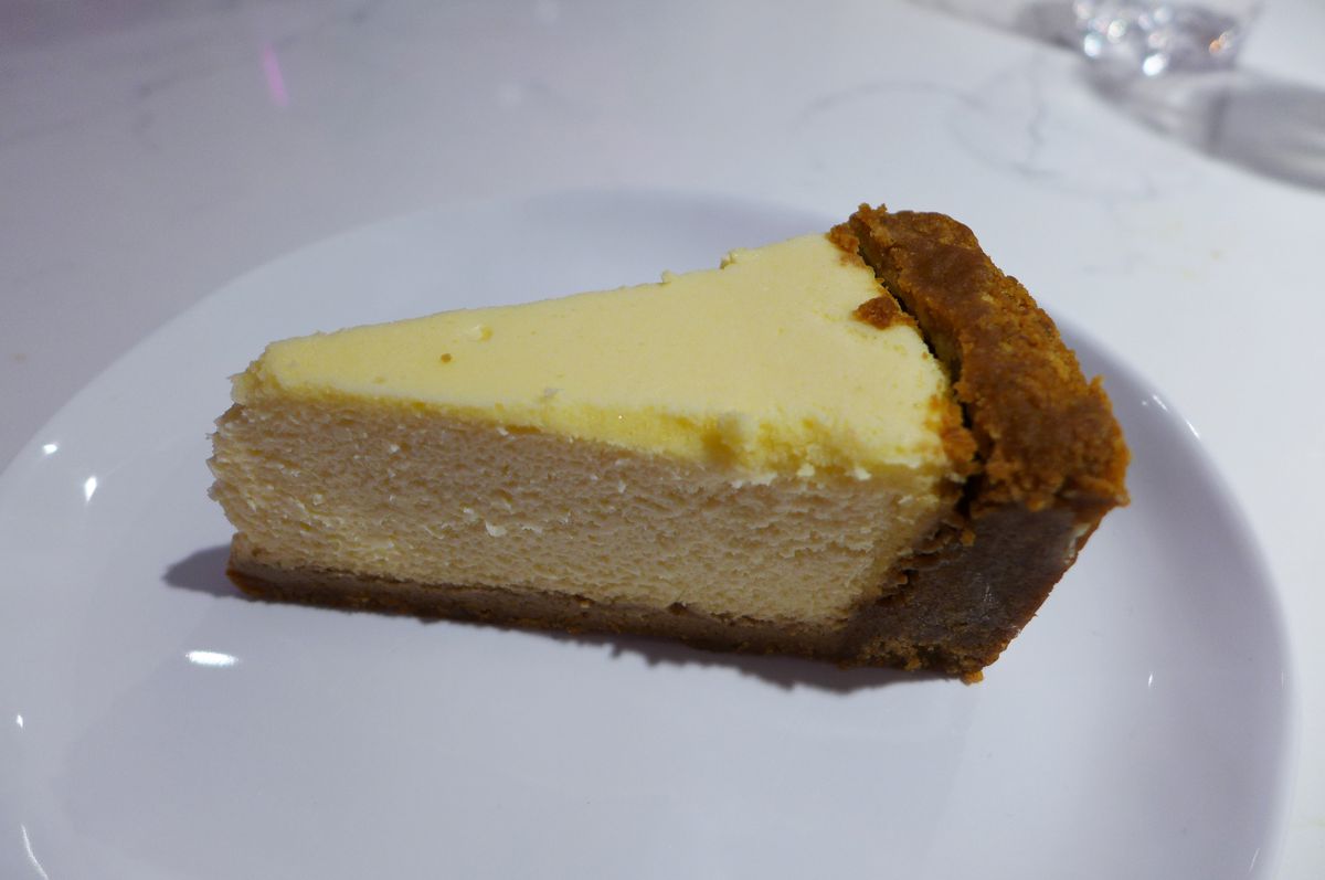 A yellow wedge of cheesecake with graham cracker crumbs.