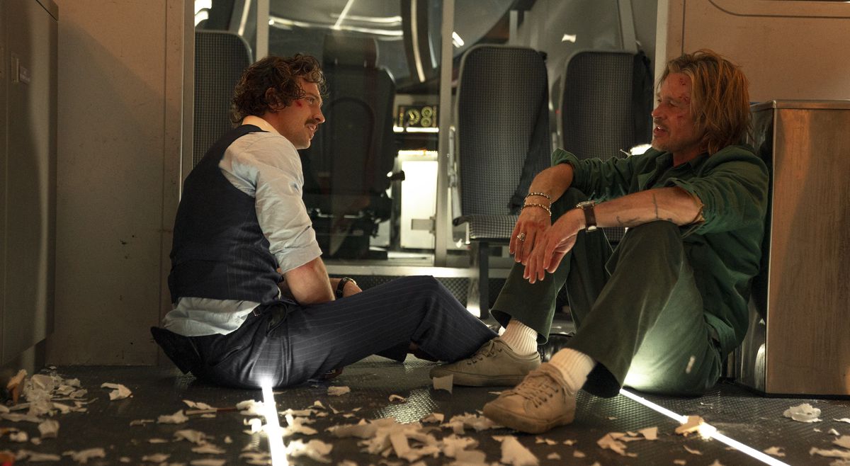 Bloodied and scruffy, Aaron Taylor-Johnson and Brad Pitt share a moment sitting on the bullet train amid piles of torn papers