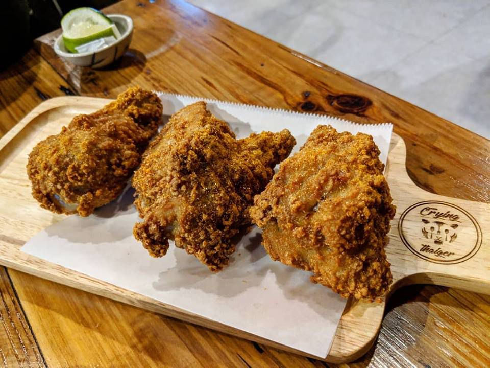 Meaty chicken wings with a breaded, fried crust sit on a wooden platter on a wooden table