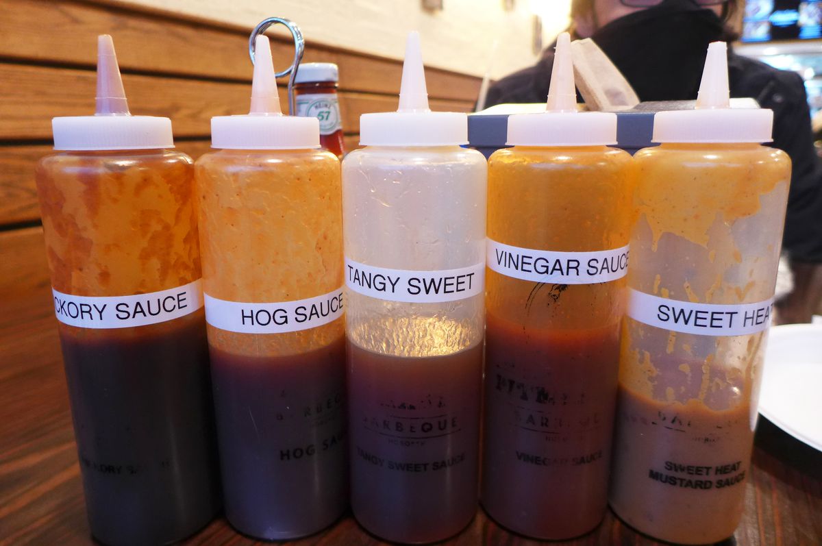 Five plastic squeeze bottles of sauce in shades ranging from yellow to red to brown.