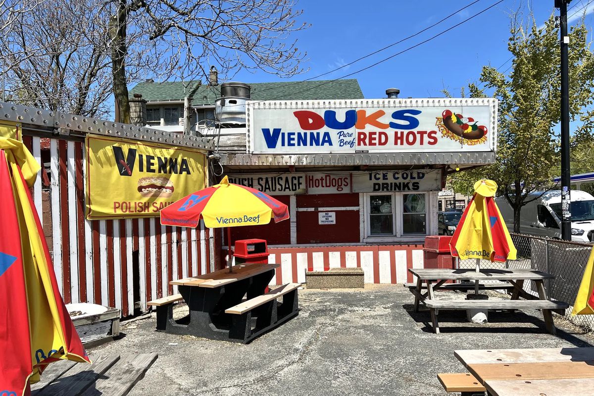 A hot dog stand with a large sign that reads “Duk’s Vienna Pure Beef Red Hots.”
