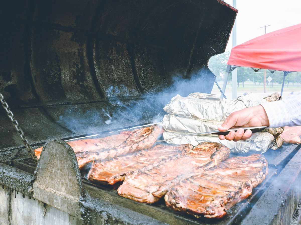 A hand reaches over to turn ribs on a smoking grill.