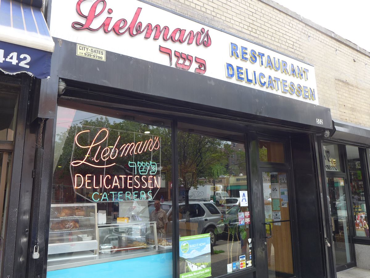 The glass window of a storefront with neon letters that read: “Liebman’s Delicatessen, Caterers.”
