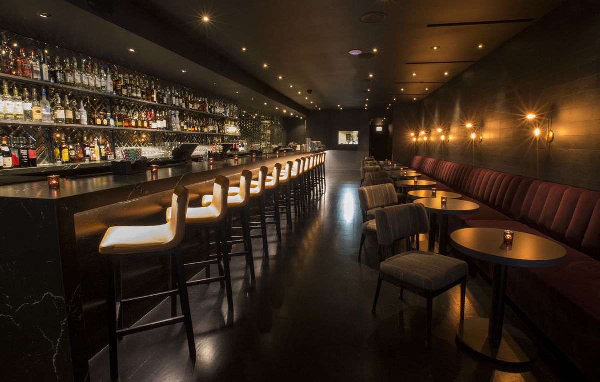 A long, narrow bar space across from a line of tables along a wall banquette.