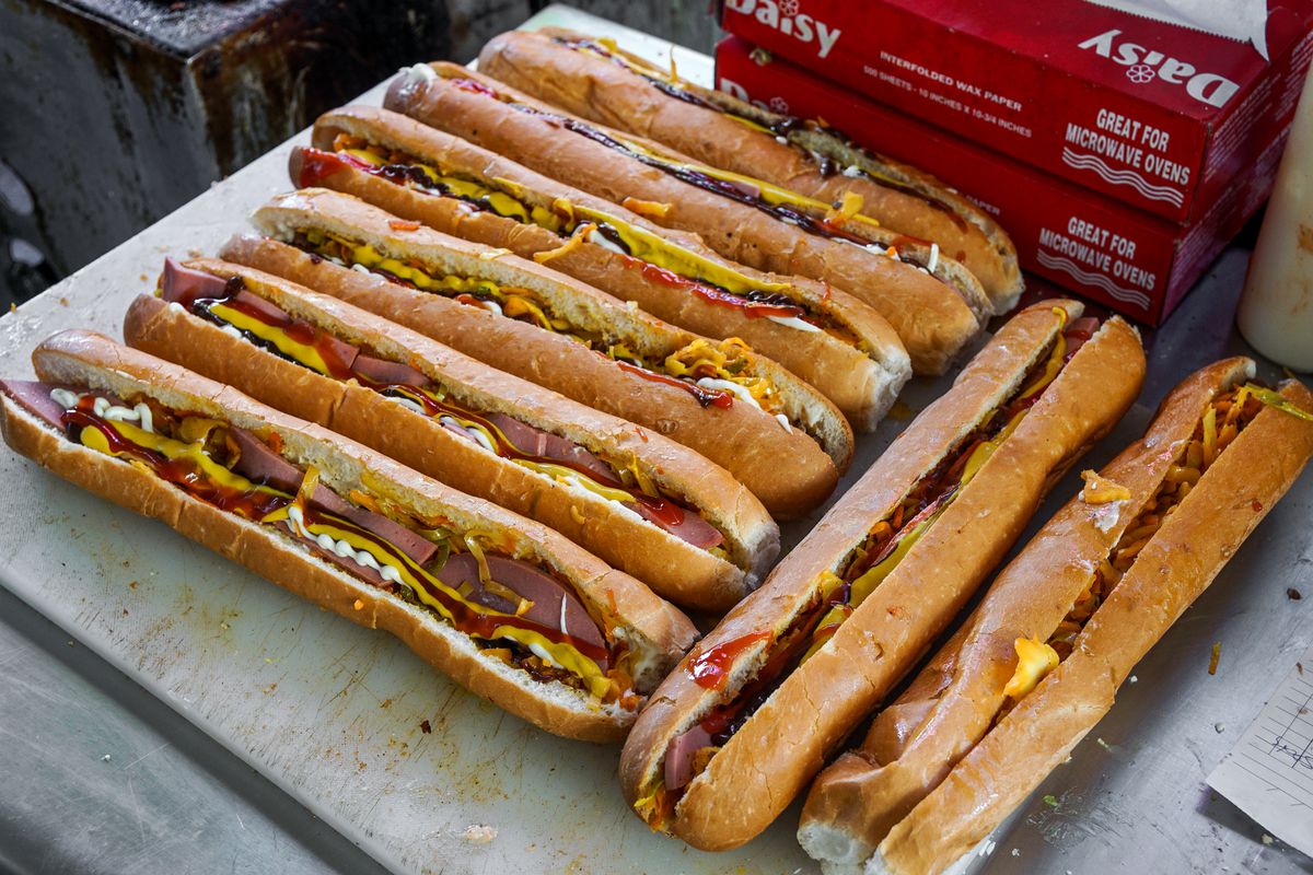 Long cut rolls with slices of meat, condiments, and cheese sit side by side at a daytime street food vendor market in Los Angeles.