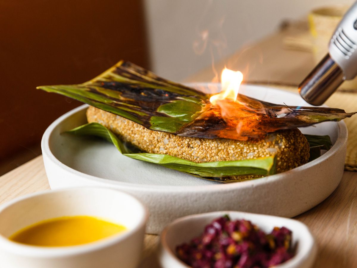A torch lighting up a green banana leaf placed on top of a burrito-like roll