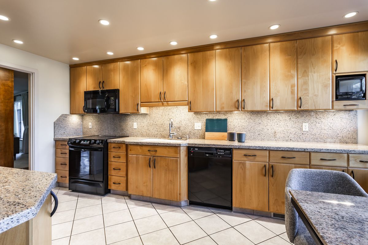A kitchen has oak cabinets, black appliances, and speckled counter tops. 