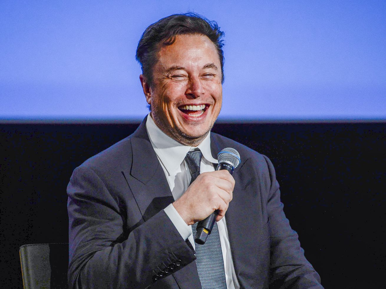 Elon Musk holding a microphone and laughing.