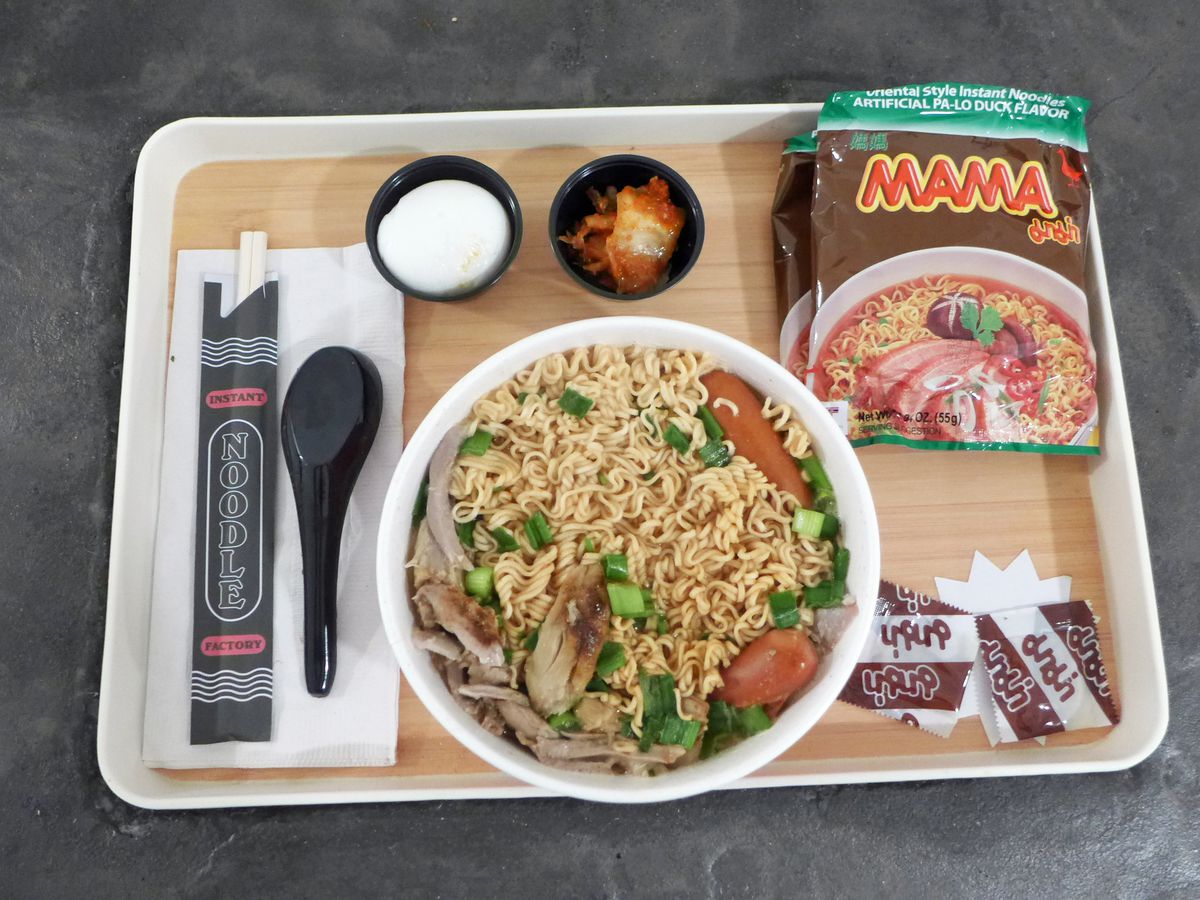 A bowl of noodles on a tray with other ingredients around it.