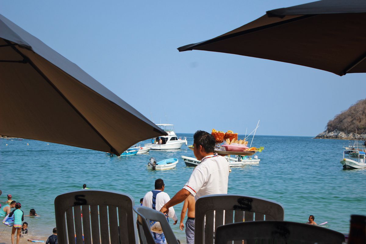 A server carries trays of shrimp cocktail on a beach.