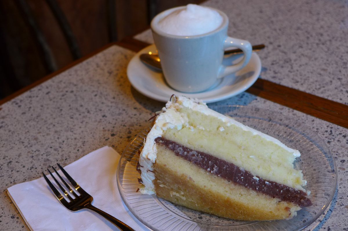 A slice of cake and a foamy cup of coffee.